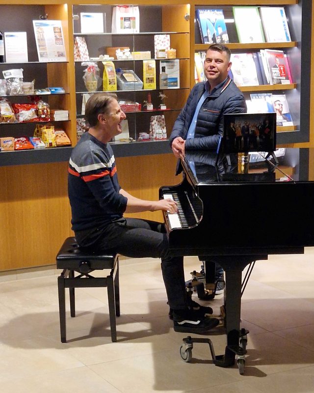 Ein Mann spielt Klavier und ein Mann steht daneben