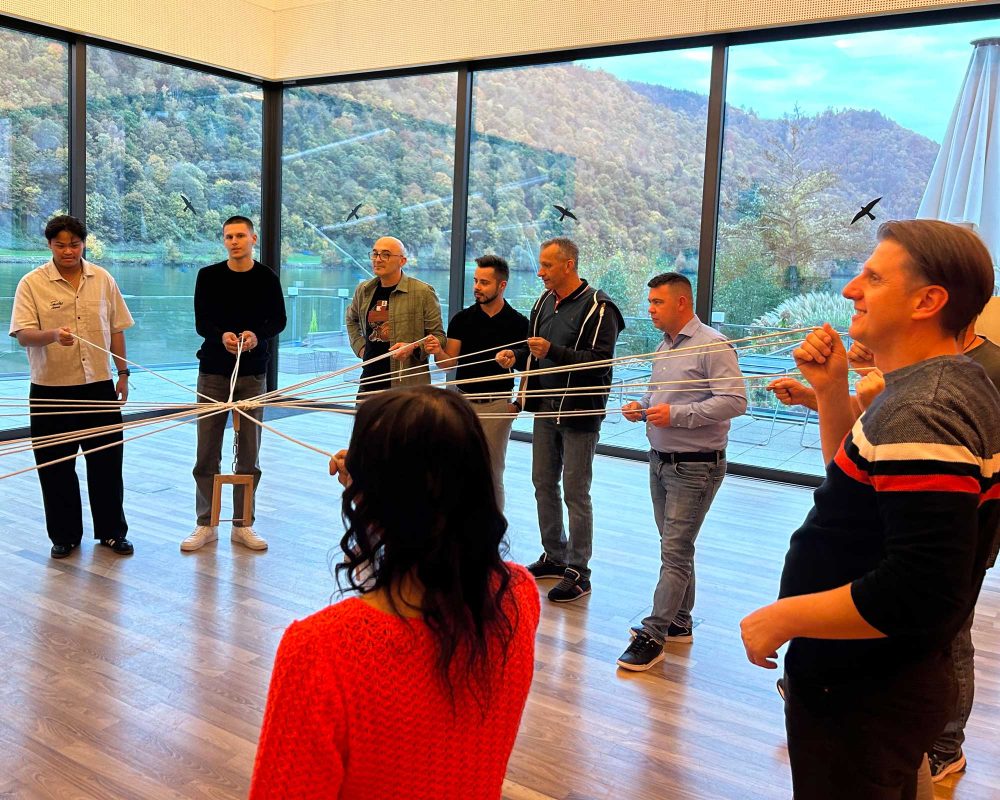 Eine Gruppe von Personen steht in einem Kreis und zieht gemeinsam an einem Seil