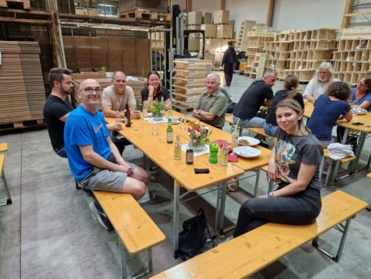 Männer und Frauen sitzen bei zwei Tischen mit Getränken und Essen darauf.